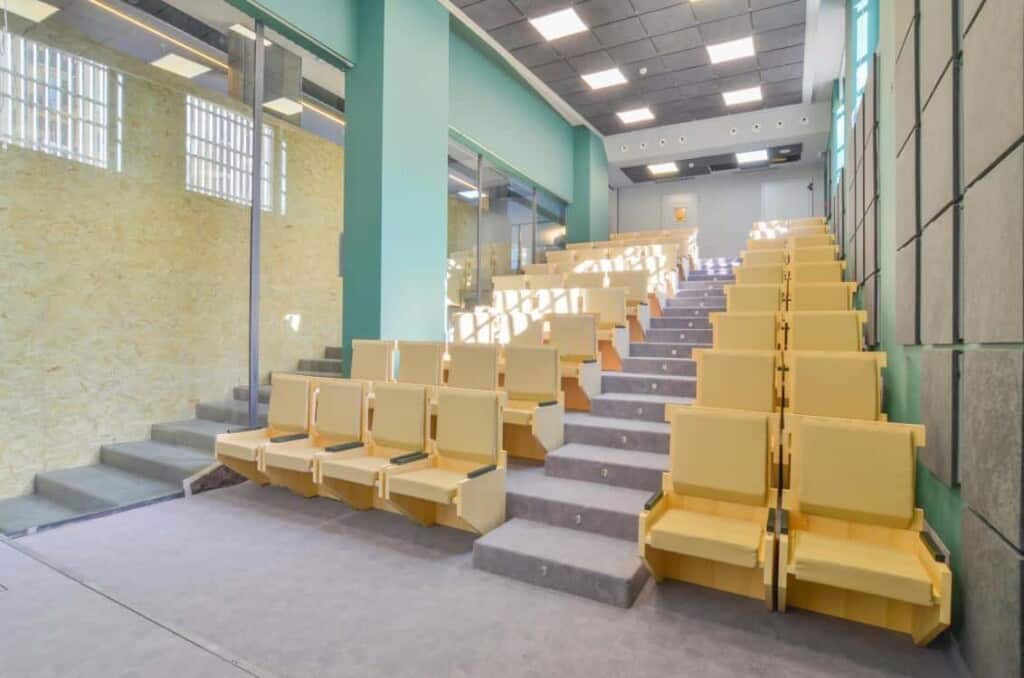 Colourful and quirky auditorium with a retro touch featuring wooden seats and radiant blue walls.