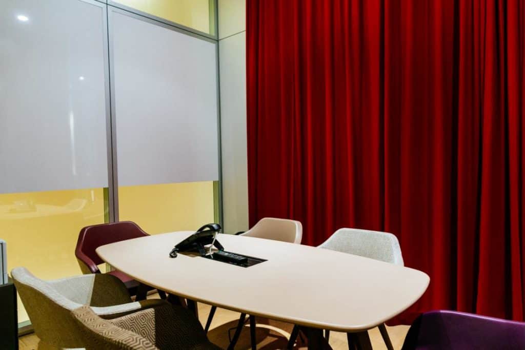 Modern meeting space with a minimalistic style featuring floor-to-ceiling windows and velvety red curtains.