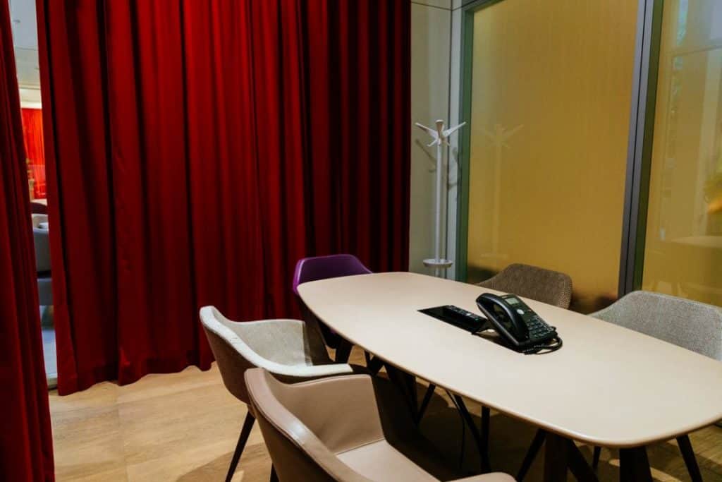Modern meeting space with a minimalistic style featuring floor-to-ceiling windows and velvety red curtains.